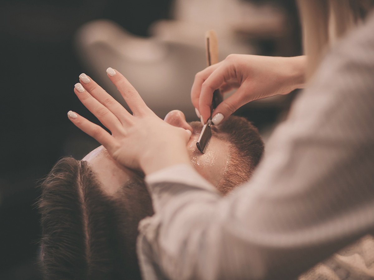 barber shaving man's face with straight razor