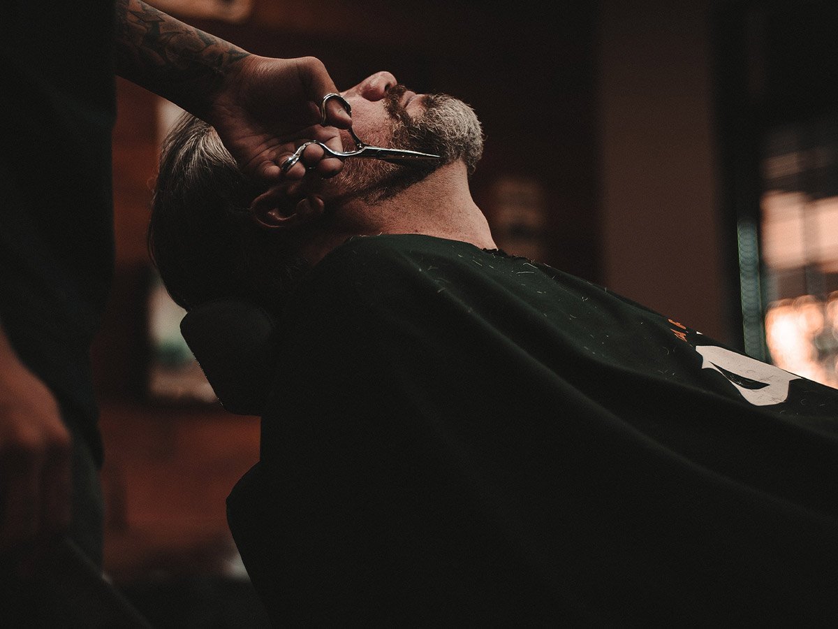image of barber using cutting shears to trim another man’s beard