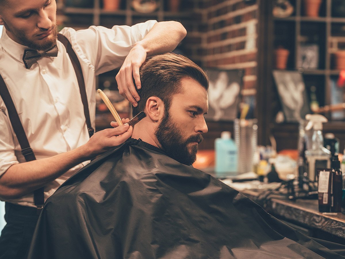 side profile image of man in barber chair getting neck edged with a razor by barber